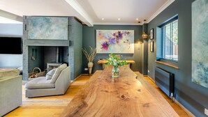 Una sala de estar moderna con una mesa de comedor de madera, una chimenea y un cuadro abstracto grande.