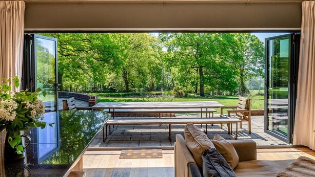 Una sala de estar moderna con un amplio ventanal que da a un patio exterior, un sofá, una mesa de centro y una mesa de comedor.