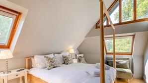 Un dormitorio con una cama de madera con dosel, una mesita de noche, una lámpara y vistas a árboles a través de las ventanas.