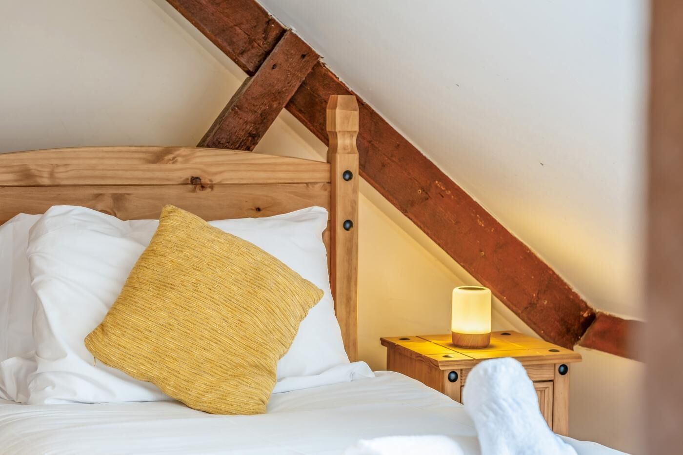 A bedroom with a wooden ceiling, a bed with white bedding, a yellow pillow, and a bedside table with a lit lamp.