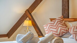 Et soveværelse med træloft, en seng med hvide sengetøj, en lampe og puder med mønster.