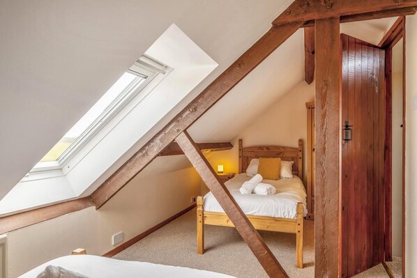 Une chambre avec un plafond en pente, un cadre de lit en bois et un puits de lumière.