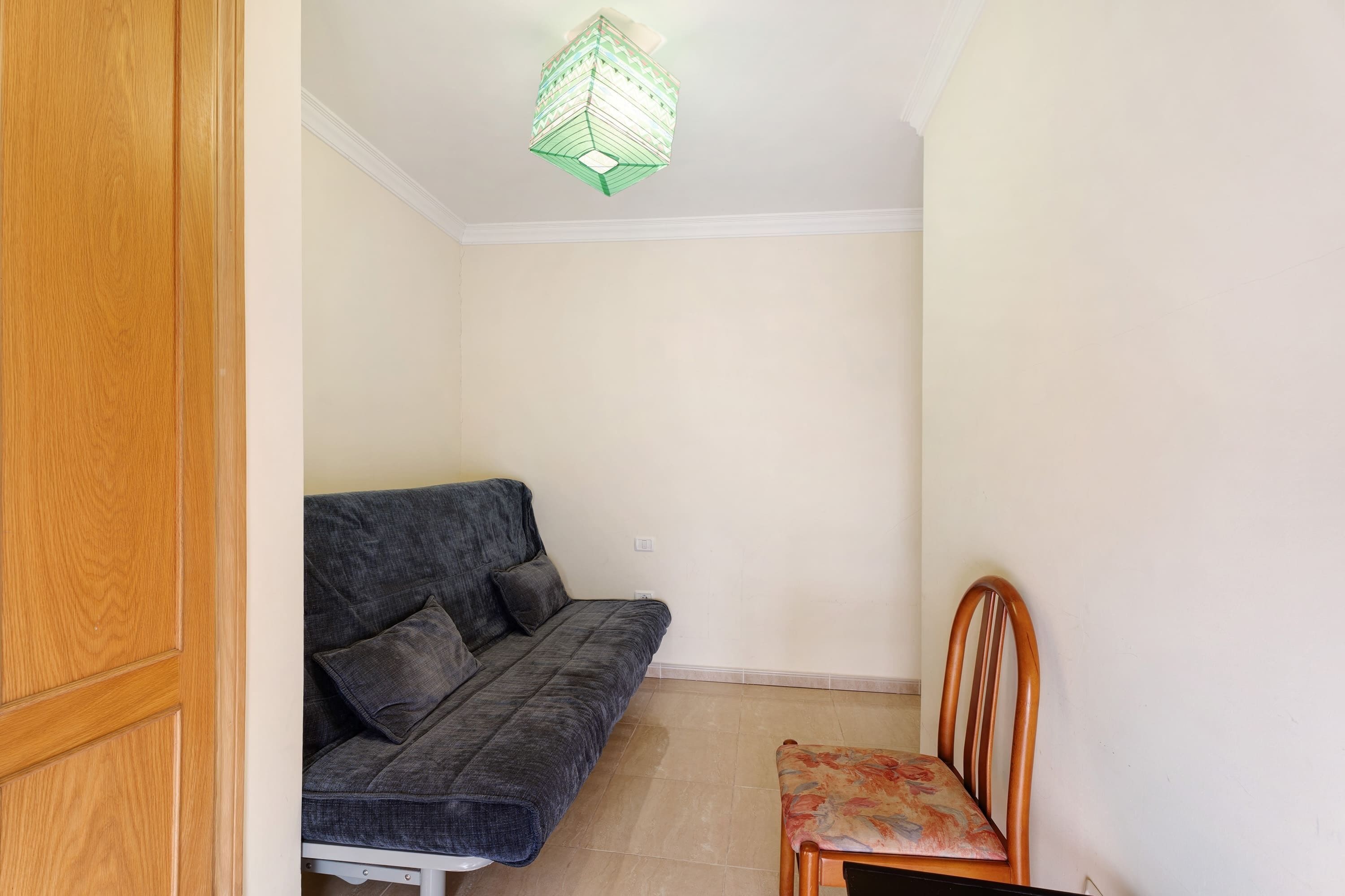 Ein Zimmer mit Holztür, grauem Sofa, Holzstuhl und Pendelleuchte.