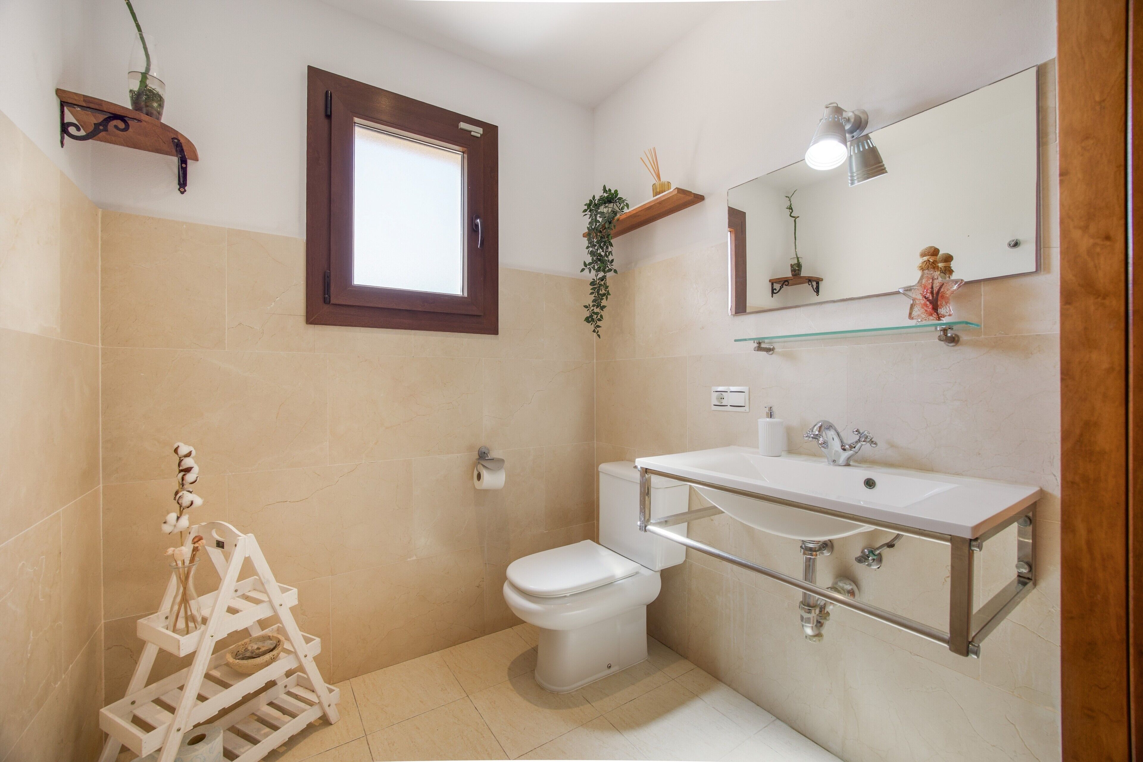 A bathroom with a toilet, sink, mirror, and a window.