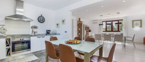 Eine moderne Küche mit einem Backofen von Bosch, ein Essbereich mit einem Glastisch und braunen Stühlen sowie ein Wohnbereich mit einem Holzkabinett und einem großen Fenster.