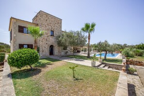 A stone building with a pool, surrounded by greenery and a clear sky.
