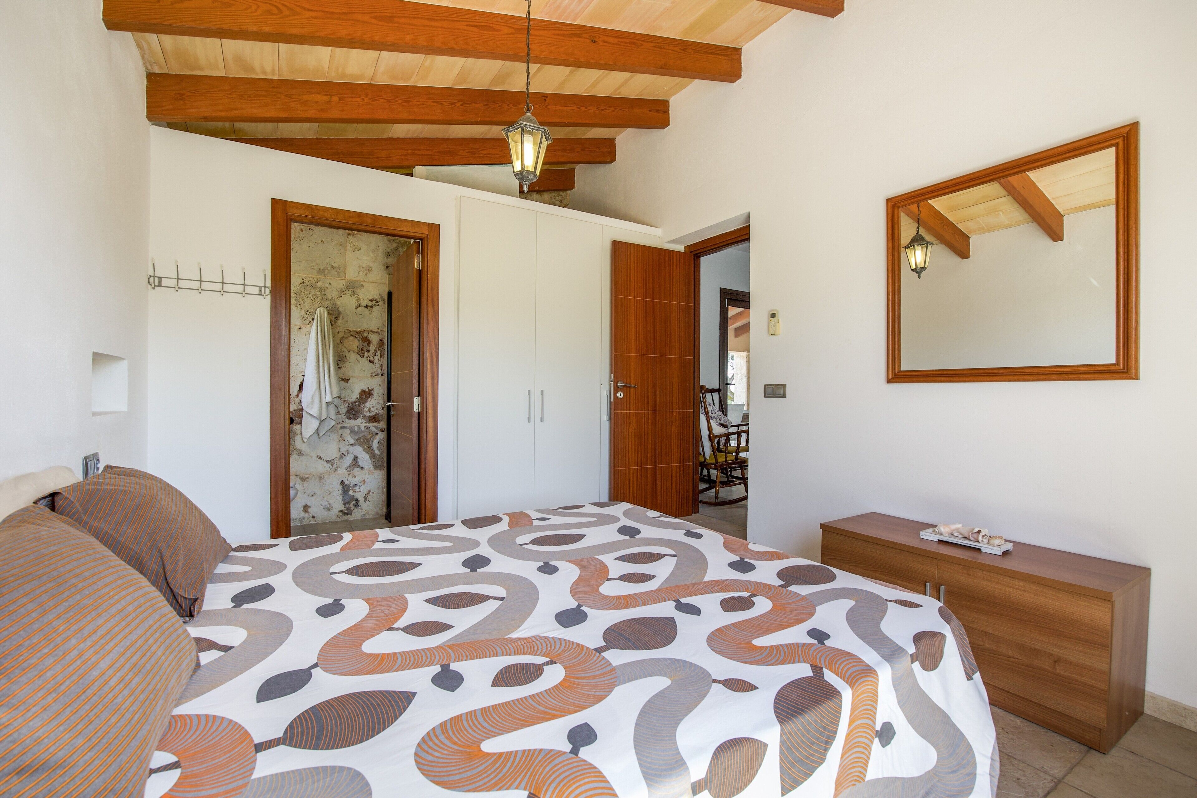 Een slaapkamer met een bed, een dressoir, een spiegel en een kledingkast.