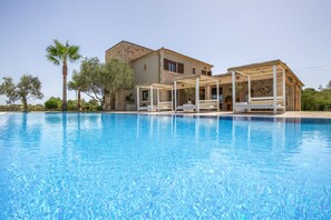 Una piscina con un pérgola y un edificio de fachada de piedra.