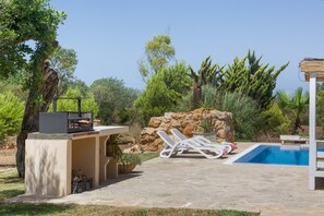 Zona de piscina con una parrilla, sillas de descanso y un muro de piedra.