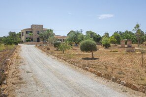 A rural road leading to a stone building with a tiled roof, surrounded by dry grass and scattered trees. - Country House 'Es Trenc' with Private Pool, Wi-Fi, and Air Conditioning (El Palmer)