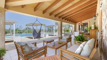 Un espacio de estar al aire libre techado con muebles de madera, una hamaca colgante y vistas a una piscina.