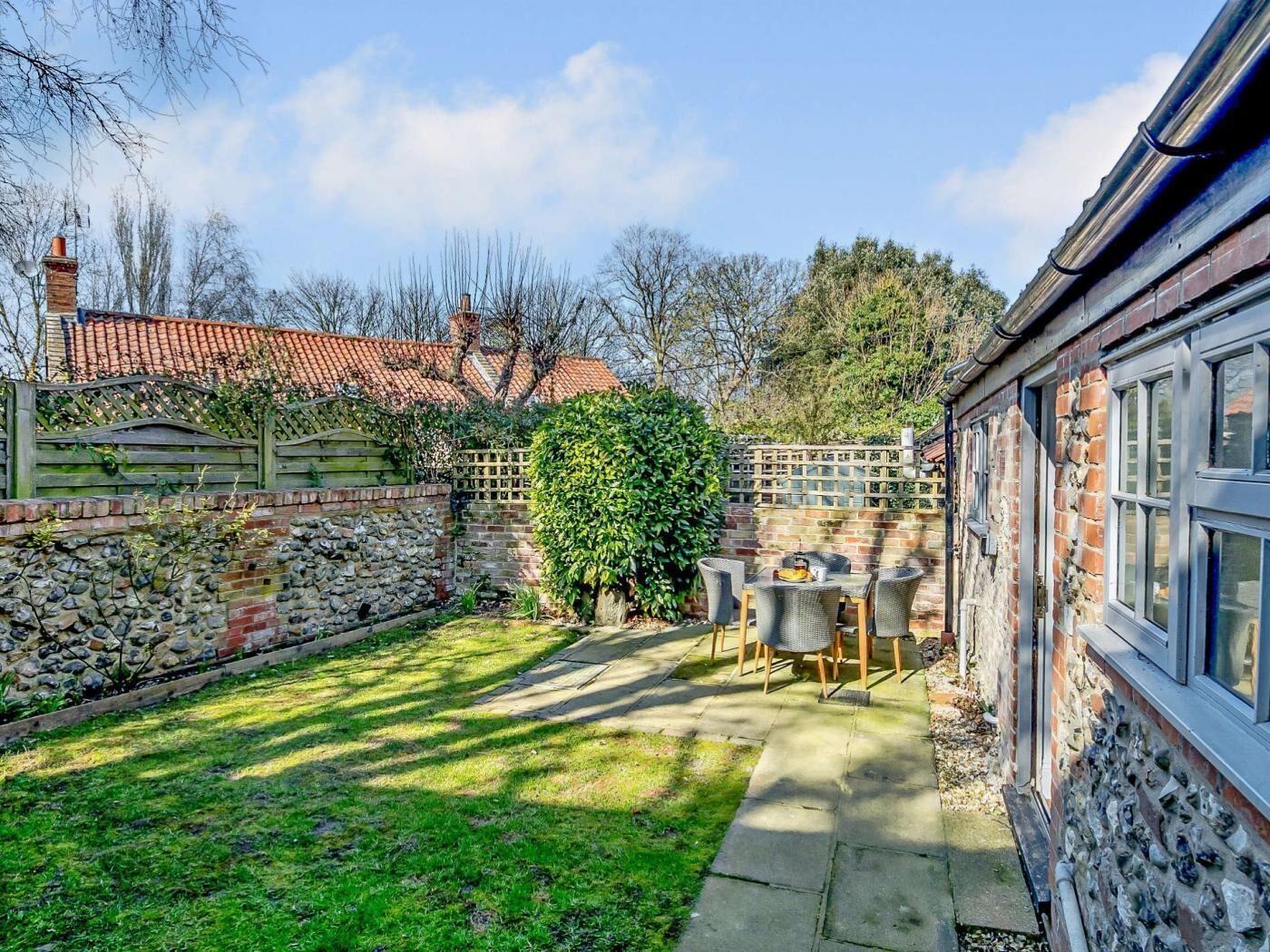 A courtyard with a stone wall, a wooden fence, a brick house, and a table with chairs.