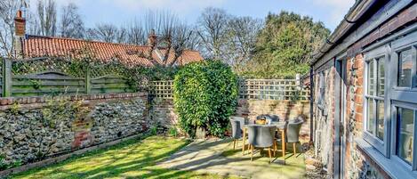 A courtyard with a stone wall, a wooden fence, a brick house, and a table with chairs.