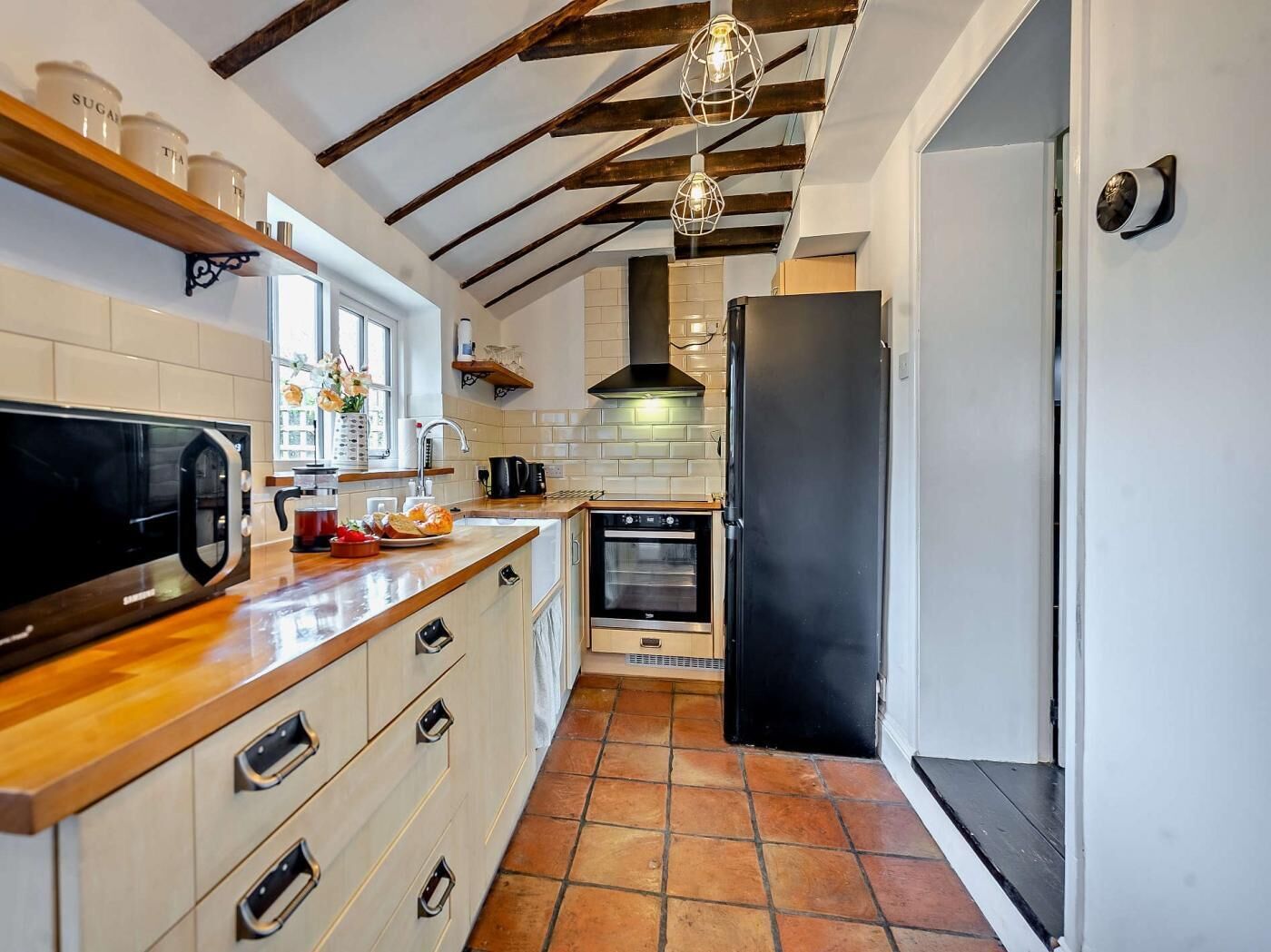 Una cocina con refrigerador negro, horno, microondas, gabinetes de madera y una lámpara colgante.