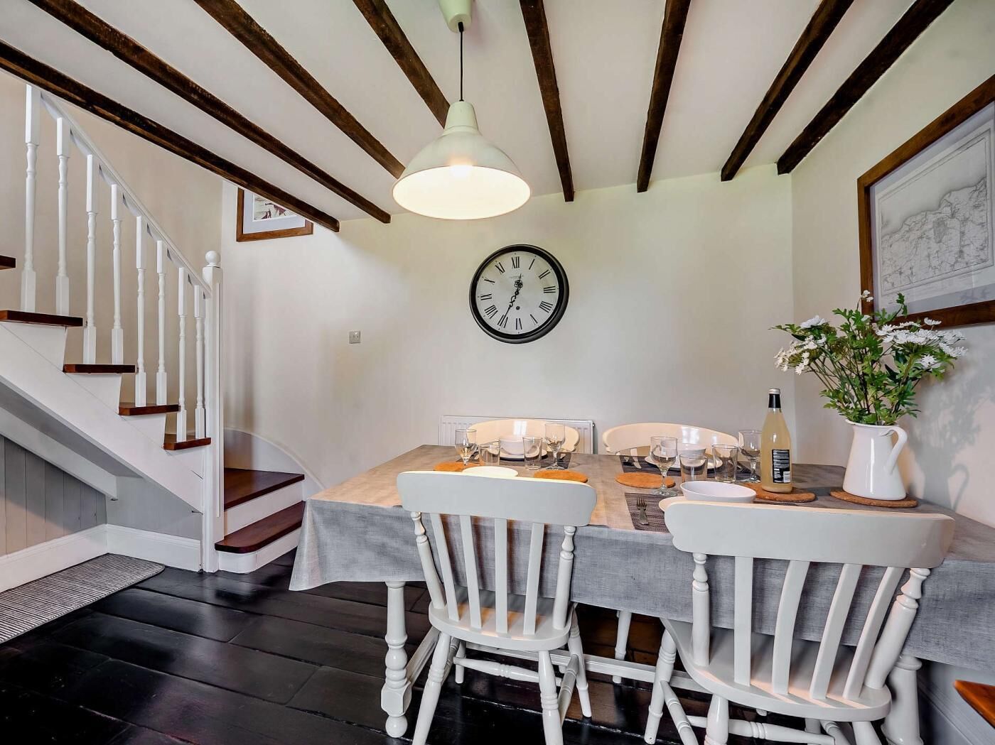A dining area with a wooden staircase, a dining table with chairs, a wall clock, and a potted plant.