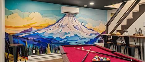 A pool table with a red felt surface, a cue stick, and a set of billiard balls.