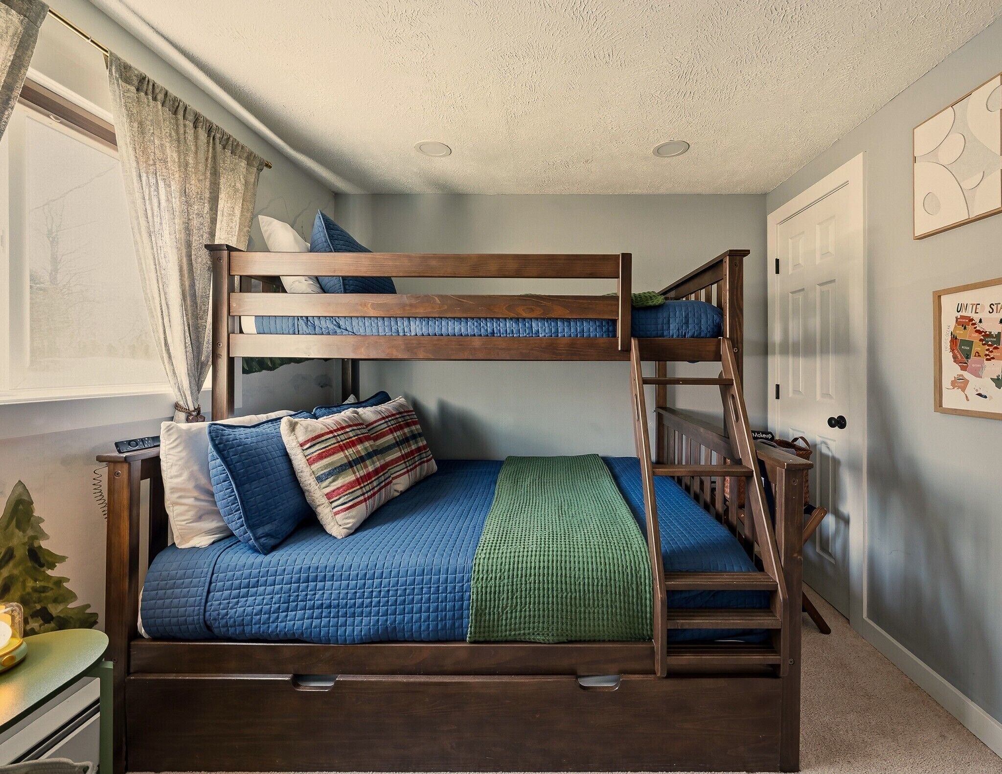 Een stapelbed met houten frame, een groene deken en blauw beddengoed.