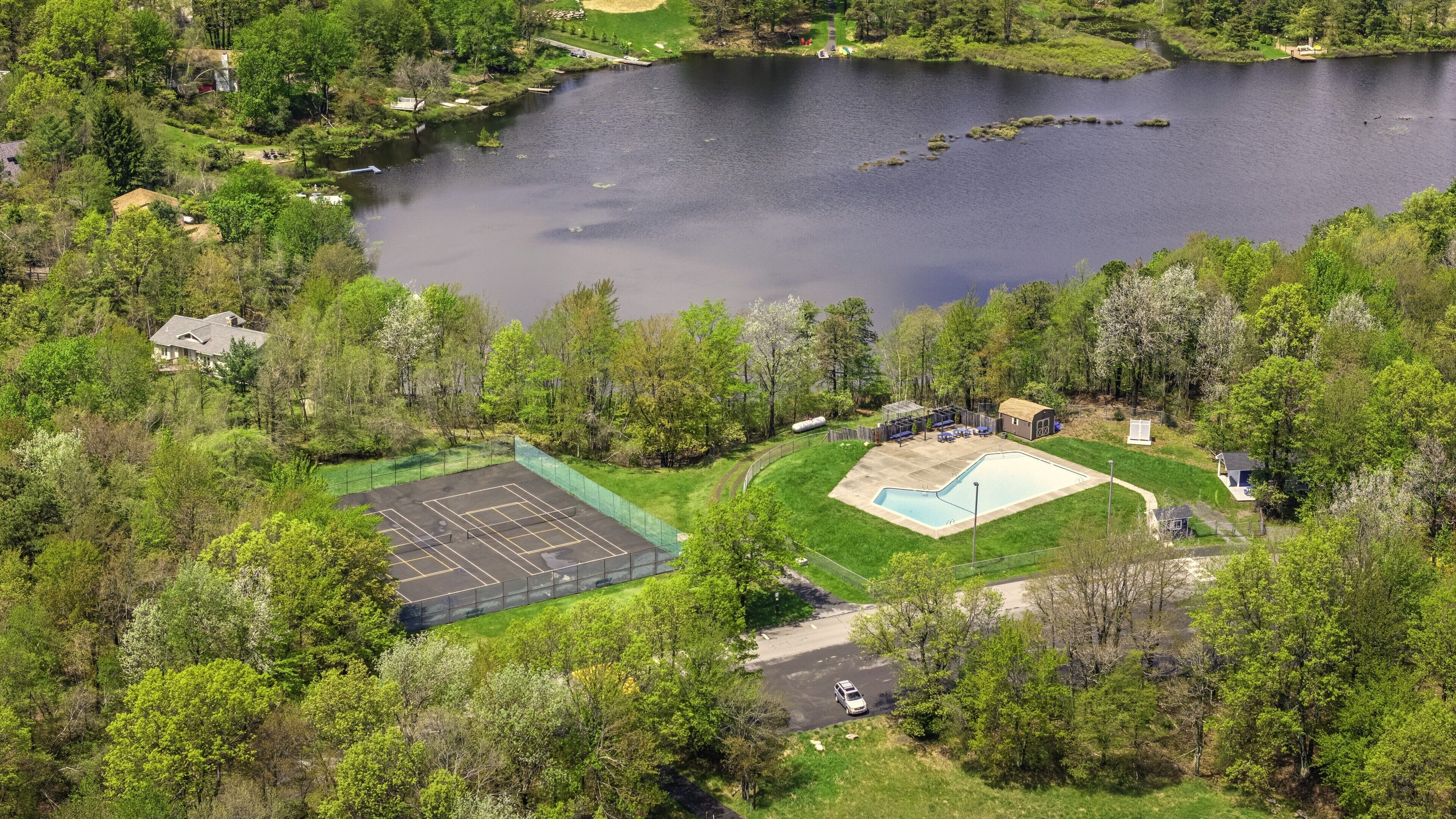 Ett flygbildsfoto av en fastighet med en swimmingpool, en tennisbana och en stor vattenyta.