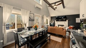 Uma cozinha moderna com fogão embutido, uma sala de jantar com mesa posta para quatro pessoas e uma sala de estar com sofá e TV.