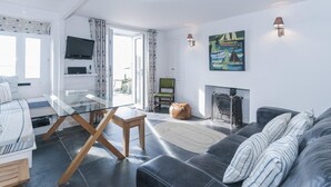 En moderne stue med et sofabord i glas, en sofa, en pejs og et tv ophængt på væggen.