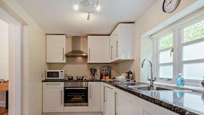 A modern kitchen with white cabinets, a stainless steel range hood, a microwave, and a sink with a window above it. - 3 Bed in Sturminster Newton (oc-rcorn) (Sturminster Newton)