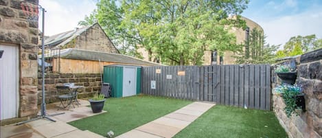 A backyard with a stone wall, a wooden fence, a green lawn, and a shed.