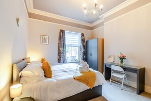 A hotel room with a bed, a desk, a chair, a wardrobe, and a window with curtains. - 1 Bed in Harrogate (oc-hh055) (Harrogate)