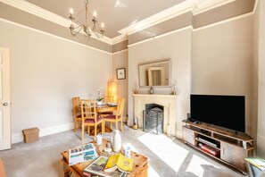 A living room with a fireplace, a television, and a dining area with chairs and a table. - 1 Bed in Harrogate (oc-hh055) (Harrogate)
