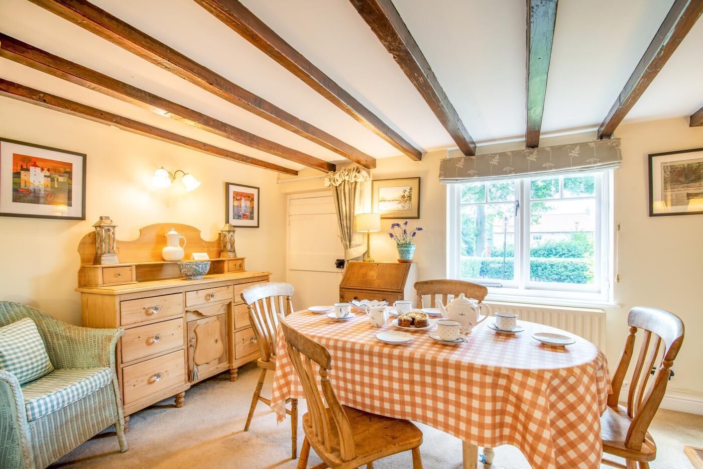 A dining area with a checkered tablecloth, wooden chairs, a wooden cabinet, and a window with a view of greenery.