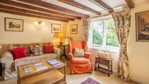 A cozy living room with a sofa, armchair, and coffee table, wooden beams on the ceiling, and a window with curtains. - 2 Bed in Northallerton (oc-g0172) (Thimbleby)