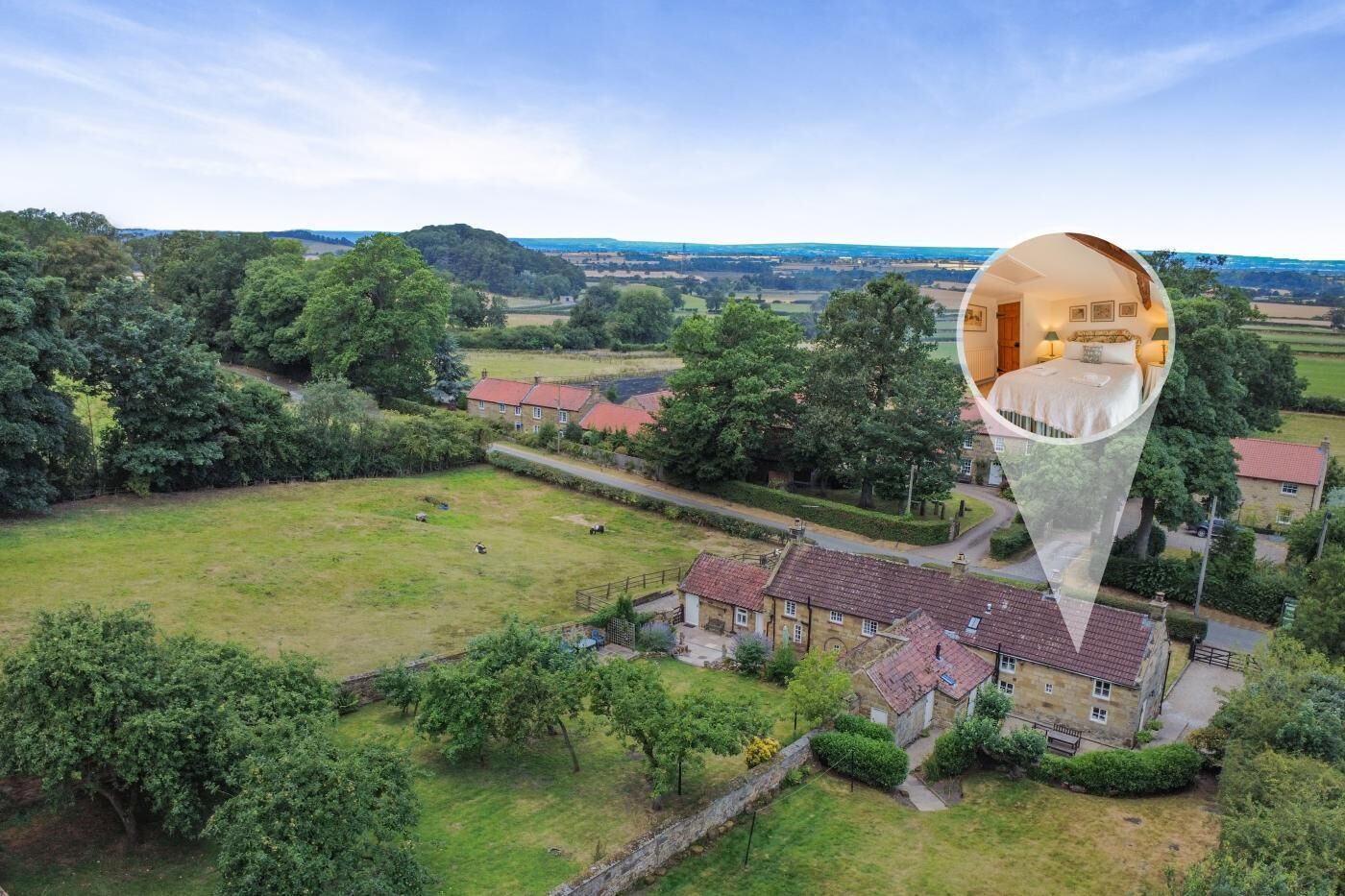 An aerial view of a rural property with a large lawn, a stone wall, and a cluster of houses with red-tiled roofs.
