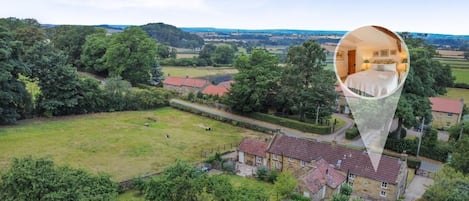 An aerial view of a rural property with a large lawn, a stone wall, and a cluster of houses with red-tiled roofs.