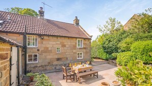 A stone house with a tiled roof, a patio with a table and chairs, and potted plants. - 2 Bed in Northallerton (oc-g0172) (Thimbleby)