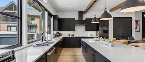 A modern kitchen with a central island, black cabinets, and pendant lighting.