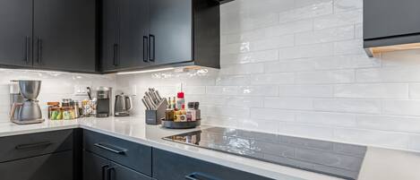 A modern kitchen with black cabinets, a white countertop, and a stainless steel range hood.