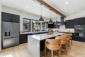 A modern kitchen with a central island, bar stools, stainless steel appliances, and pendant lighting. - The Riverstone | Luxury Alcove • Kindred • Ski-In/Out • Spa • Heated Garage (Keystone)