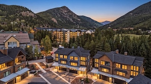 A modern resort with multiple buildings, a parking area, and a mountainous backdrop. - The Riverstone | Luxury Alcove • Kindred • Ski-In/Out • Spa • Heated Garage (Keystone)