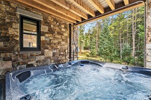 A hot tub with a stone wall backdrop and a window overlooking a forest. - The Riverstone | Luxury Alcove • Kindred • Ski-In/Out • Spa • Heated Garage (Keystone)
