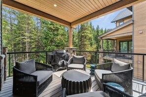 A covered deck with outdoor furniture, a grill, and a view of a forested area. - The Riverstone | Luxury Alcove • Kindred • Ski-In/Out • Spa • Heated Garage (Keystone)
