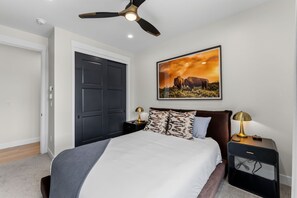 A bedroom with a bed, two bedside tables, a ceiling fan, a door, and a wall-mounted picture. - The Riverstone | Luxury Alcove • Kindred • Ski-In/Out • Spa • Heated Garage (Keystone)