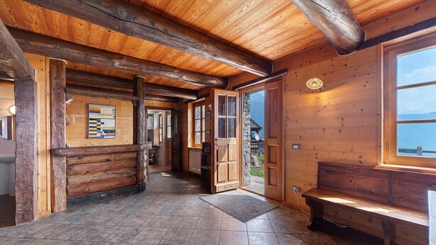 A wooden interior with a stone floor, wooden benches, and a view through an open door.