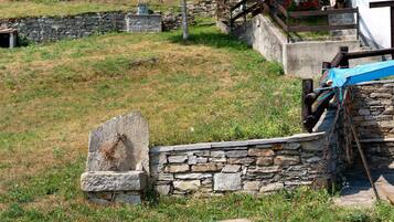 A stone wall with a gravestone, a wooden bench, and a metal structure in a grassy area.