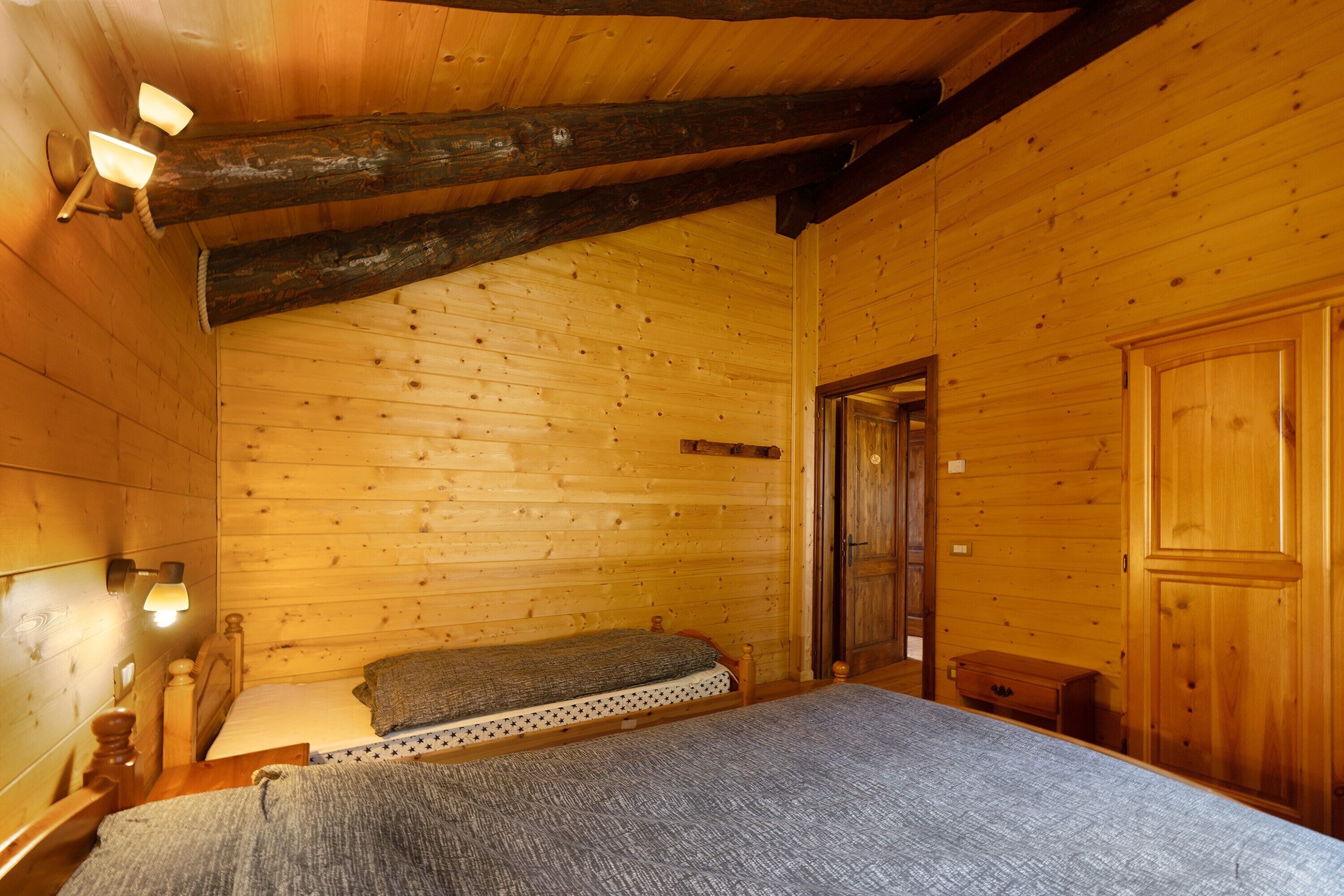 A wooden cabin room with a bed, a bench, and a door.