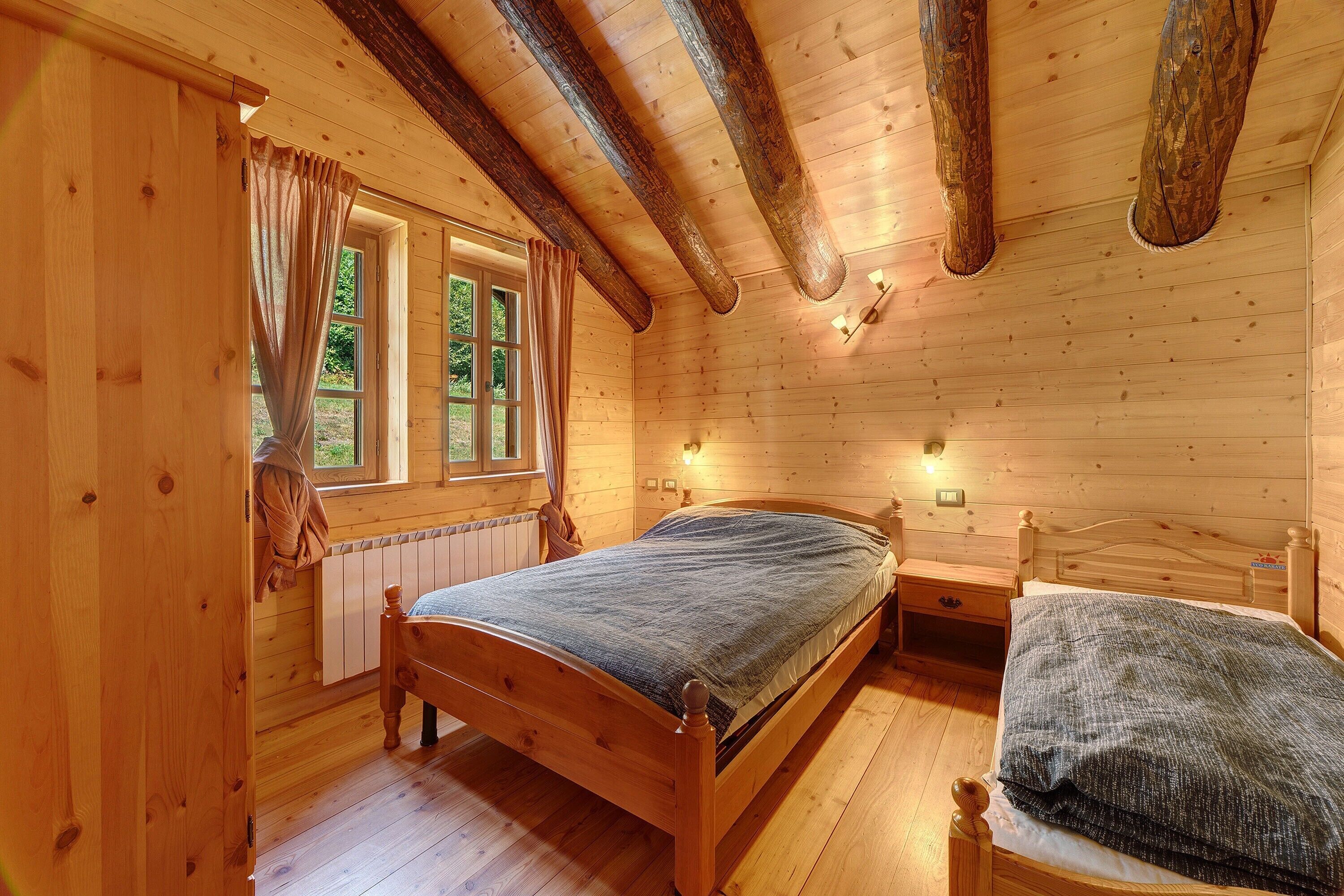 Een slaapkamer met houten wanden, voorzien van een enkel bed, een kleiner bed, een raam met gordijnen en een wandlamp.