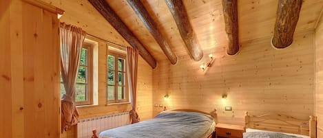 Un dormitorio de cabaña de madera con una cama individual, una cama más pequeña, una ventana con cortinas y una lámpara fijada a la pared.
