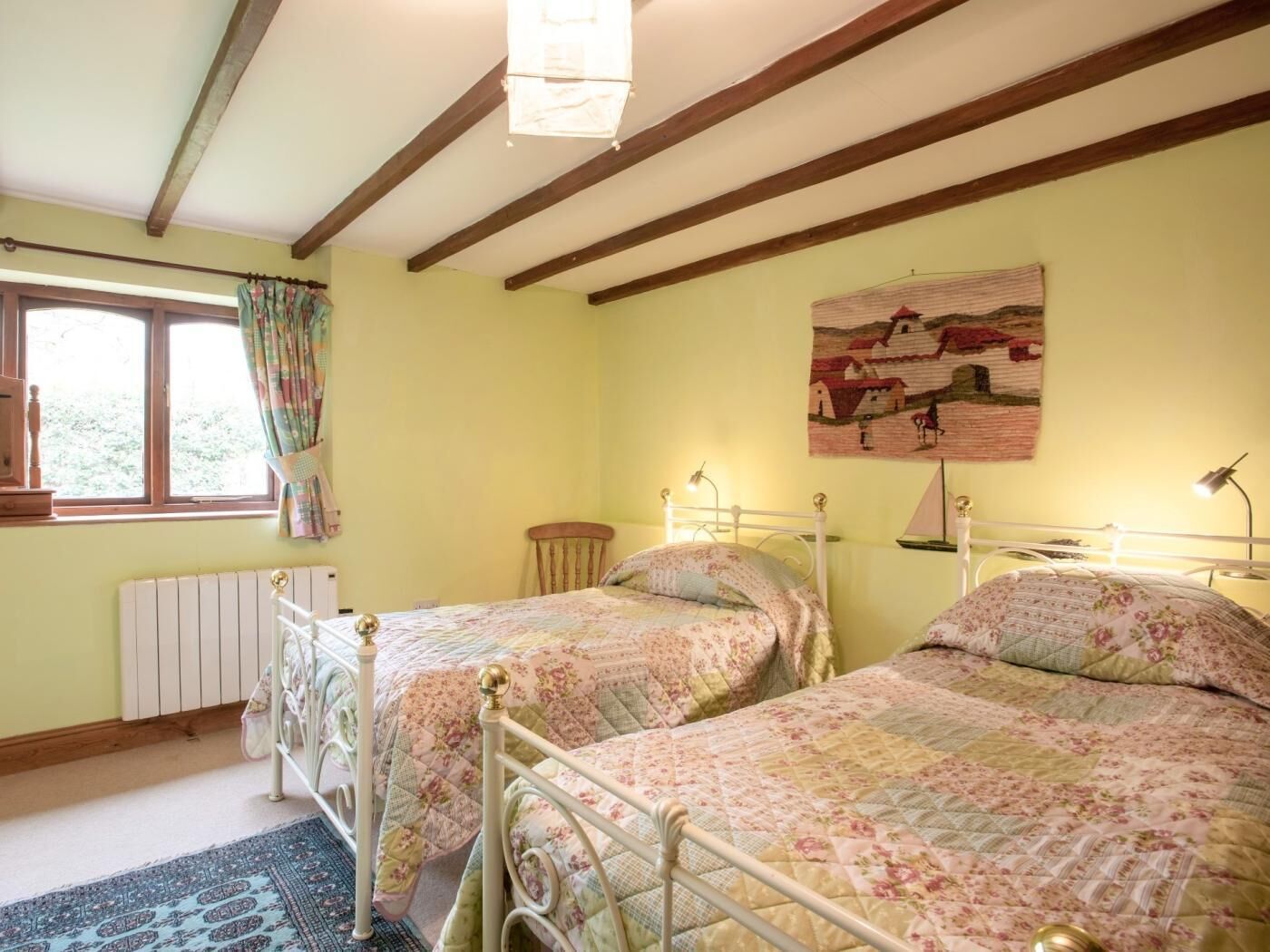 A room with two beds, a window with curtains, a radiator, and a painting on the wall.