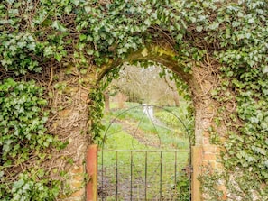 A wrought iron gate with a brick archway partially covered by ivy. - 3 Bed in South Creake (oc-kt099) (South Creake)