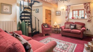 Ein gemütliches Wohnzimmer mit Treppe, roten Sofas, einem gemusterten Teppich und einem Fenster mit Vorhängen.
