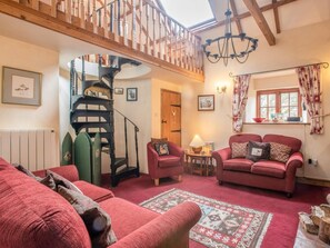 A cozy living room with a staircase, red sofas, a patterned rug, and a window with curtains. - 3 Bed in South Creake (oc-kt099) (South Creake)