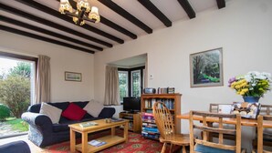A cozy living room with a sofa, coffee table, bookshelf, and a dining area with chairs. - 2 Bed in Swanage (oc-dc069) (Studland)